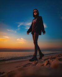 Full length of woman standing at beach against sky during sunset