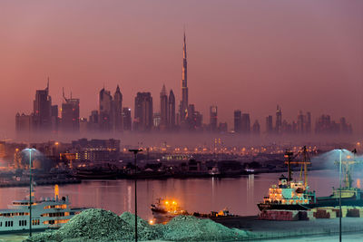 Illuminated buildings by sea at dusk