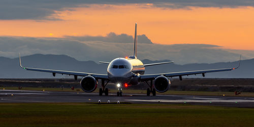 Airplane on airport runway against sky during sunrise