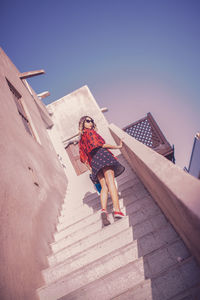 Low angle view of young woman on staircase against sky