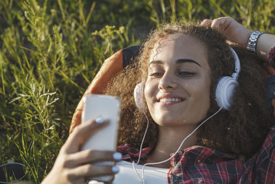 Teenage girl with backpack lying on a meadow listening music with headphones and cell phone