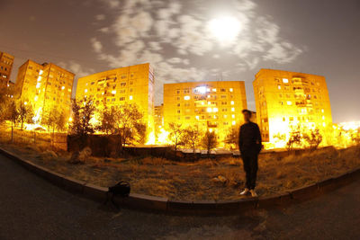 Rear view of silhouette man standing by illuminated city against sky at night