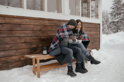 Young couple in love in the woods basking under a blanket. they drink tea from a thermos