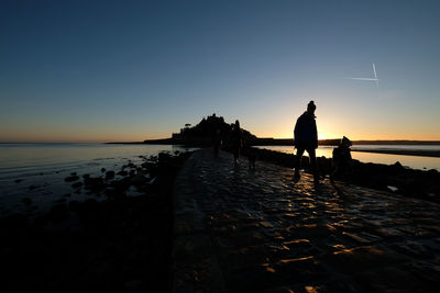 Silhouette man standing on beach against clear sky during sunset