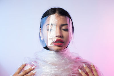 Close-up of young woman wrapped in plastic against colored background