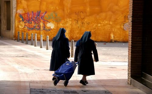 Rear view of nuns pulling luggage on walkway