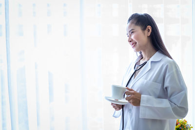 Young woman smiling while standing against window