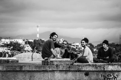 People sitting on retaining wall against sky