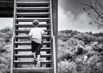 Rear view of boy climbing wooden steps outdoors