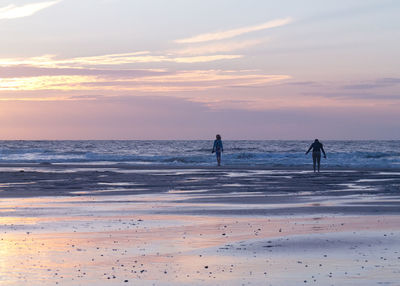 People on beach against sky during sunset