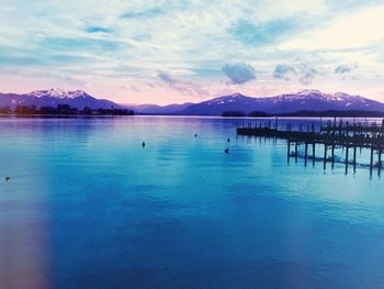 Silhouette pier in river against cloudy sky at dusk