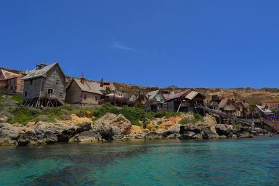 Houses by sea against buildings against clear blue sky