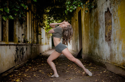 Full length of female ballet dancer dancing in alley amidst abandoned buildings