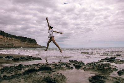 Man jumping at beach against sky