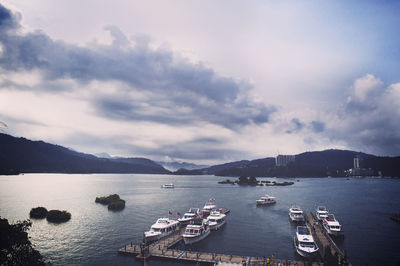 Boats moored at harbor in sea against cloudy sky