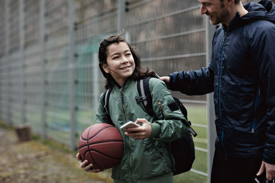 Smiling son looking at father while standing on playing field