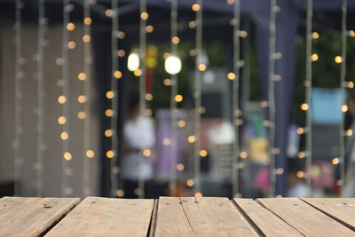 Close-up of wooden table against illuminated lights at night