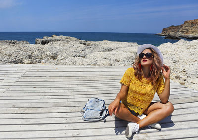 Young woman sitting on beach by sea against sky