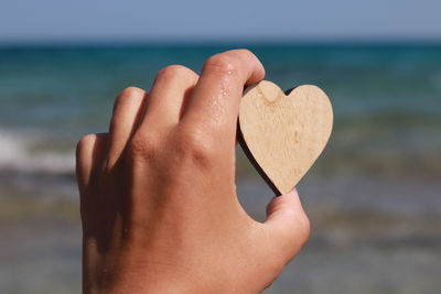 Close-up of hand holding heart shape over sea