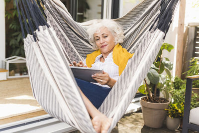 Mature woman using digital tablet while sitting on hammock at home