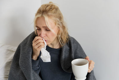 Young woman drinking coffee while sitting against white background