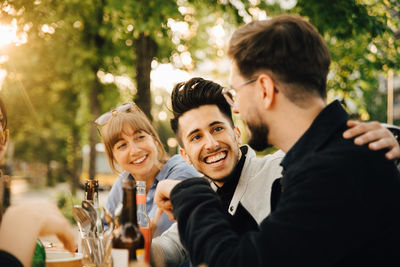 Happy young man sitting by male and female friend at social gathering