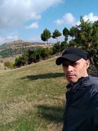 Portrait of man standing on field against sky