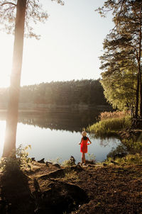 Rear view of woman standing by lake against clear sky