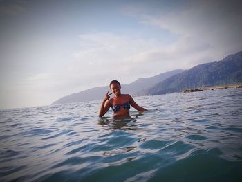 Portrait of young woman gesturing in sea against sky