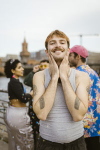 Portrait of smiling gay man touching face while standing near friends
