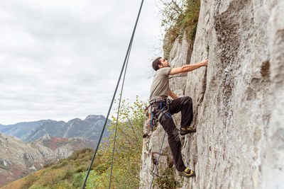 Sportive male alpinist climbing on sheer cliff in summer day