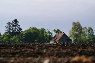 House on field by trees against sky