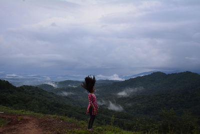Side view of woman tossing hair while standing on mountain against sky