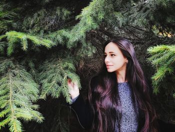 Thoughtful young woman standing against trees