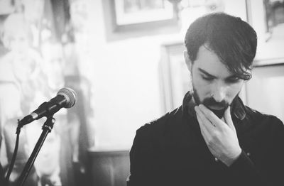 Young bearded man with hand on chin standing by microphone