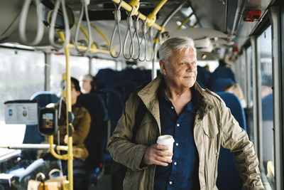 Thoughtful businessman holding disposable cup while commuting through bus
