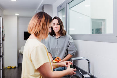 Side view of woman cleaning hand at sink in kitchen