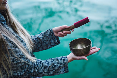 Midsection of young woman holding bowl over lake