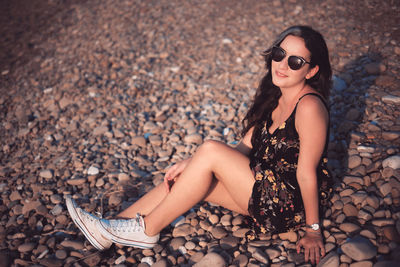 Midsection of woman wearing sunglasses on pebbles