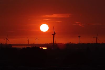 Silhouette windmill on field against orange sky