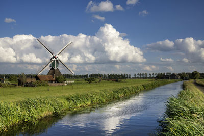 Traditional windmill on field by lake against sky