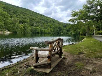 Wooden bench by lake against sky