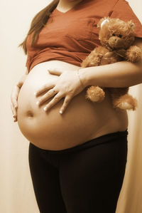 Midsection of pregnant woman with stuffed toy against gray background