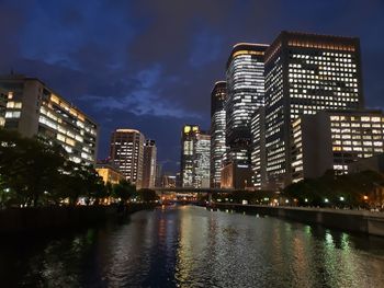 Illuminated buildings by river against sky in city at night