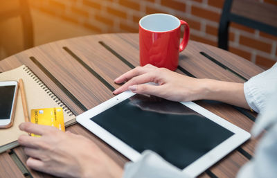 Cropped hands of woman using digital tablet while sitting at table in cafe