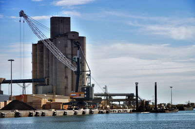 Cranes at harbor against sky