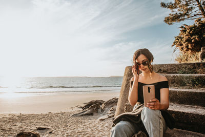 Young woman using mobile phone while sitting at beach