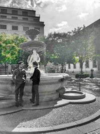 People standing by fountain in city against sky