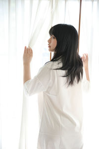 Portrait of young woman standing against curtain