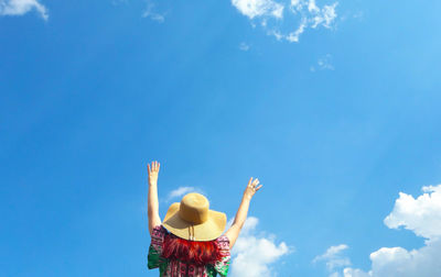 Low angle view of person with arms raised against blue sky